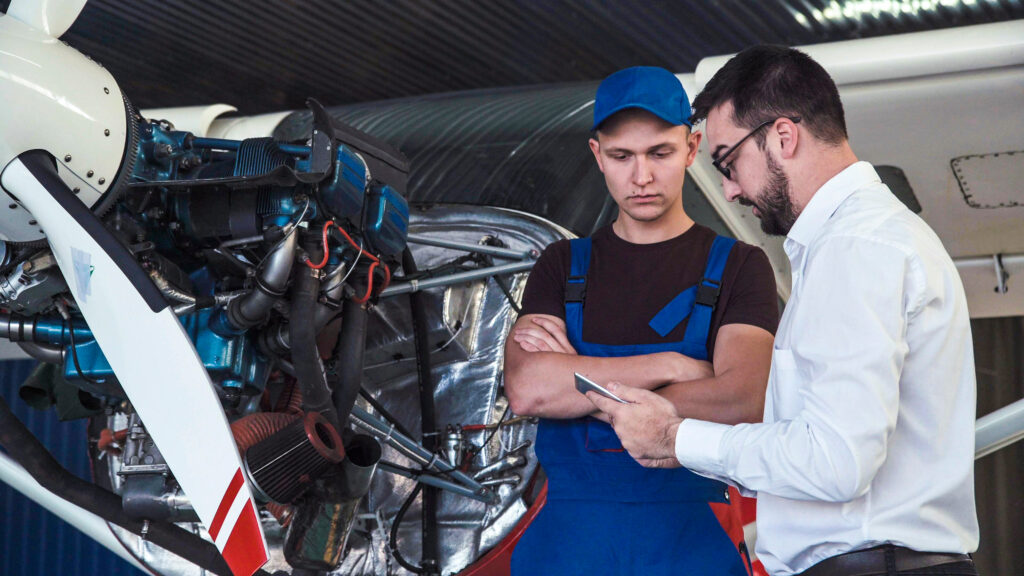 Mechanic and flight engineer having a discussion looking at a tablet-pc together as they stand in front of a small single engine aircraft in a hangar at Noble Air Charter Private Charter Flights Miami, Florida.